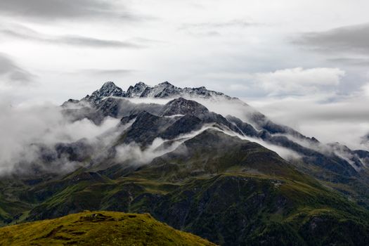 Snow-capped mountains in Korutany, Rakousko with misty clouds and lush greenery.