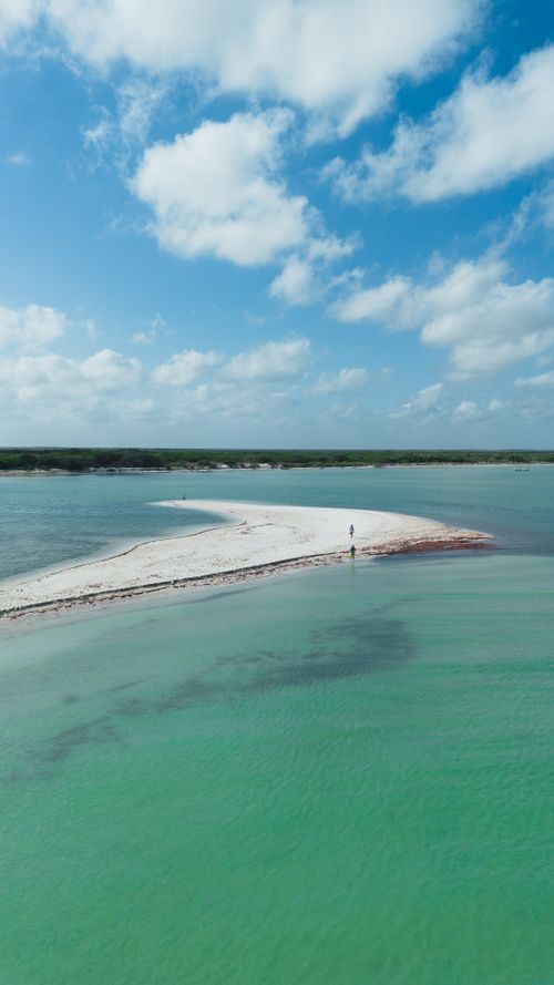 Free A solitary figure on a tranquil white sand beach with vibrant turquoise waters and a blue sky. Stock Photo
