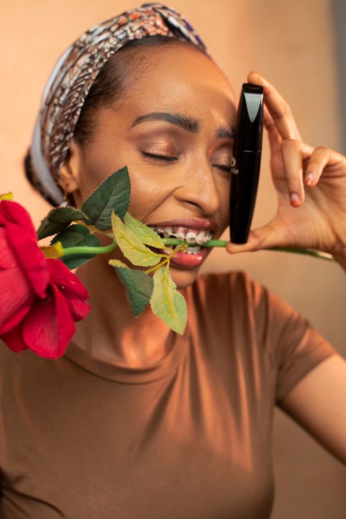 Free African woman playfully holding a rose and mascara. Vibrant expression. Stock Photo