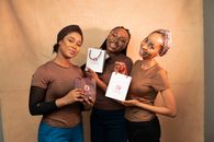 Three women smiling and holding gift bags in a cheerful setting.