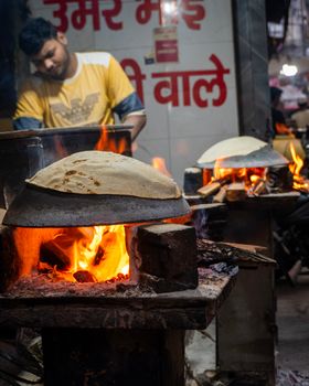 A street vendor in a busy market preparing flatbreads on open flames. Evening ambiance.