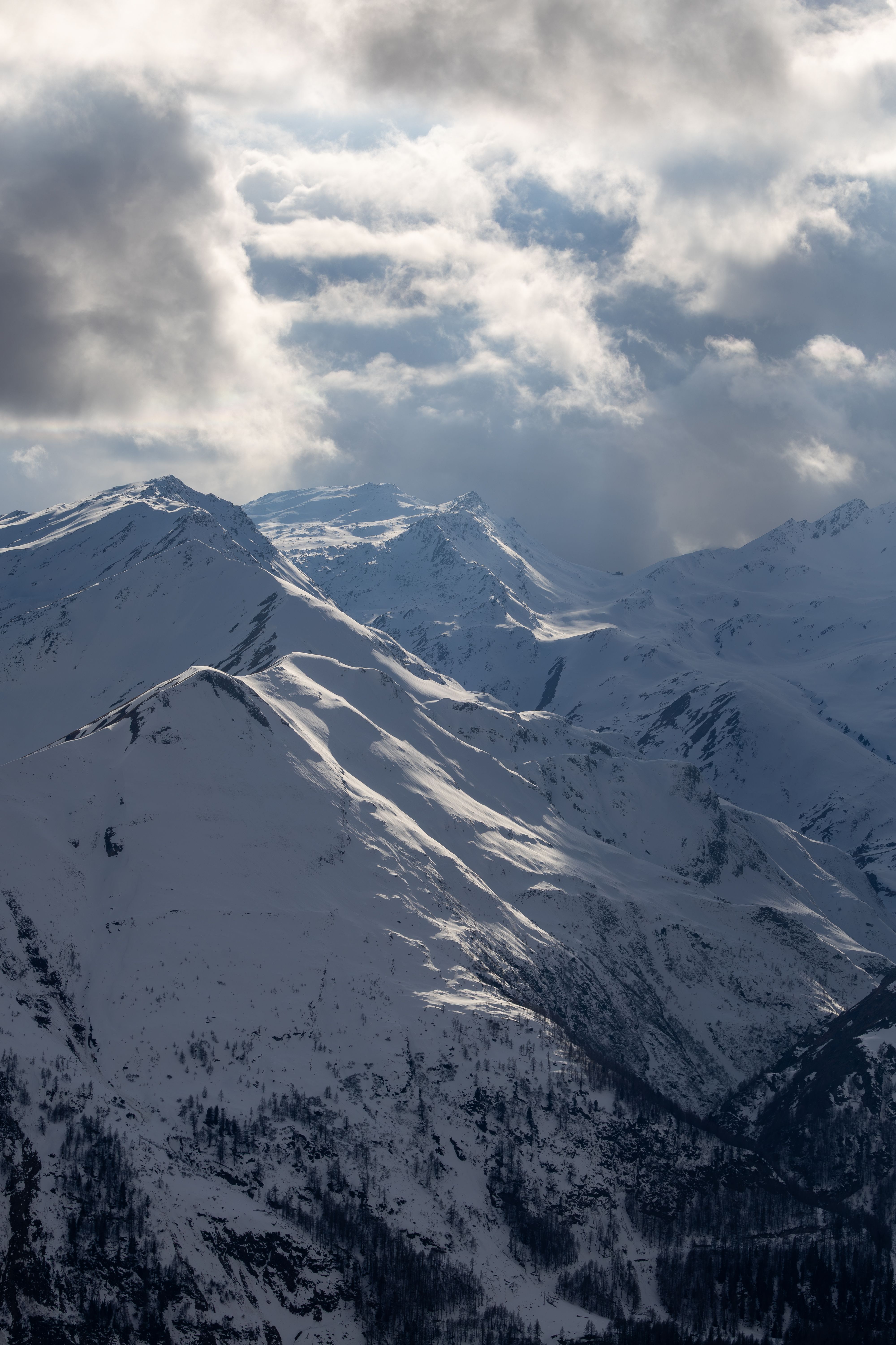 Snowy mountains under dramatic clouds in Korutany, Rakousko, showcasing winter's beauty.