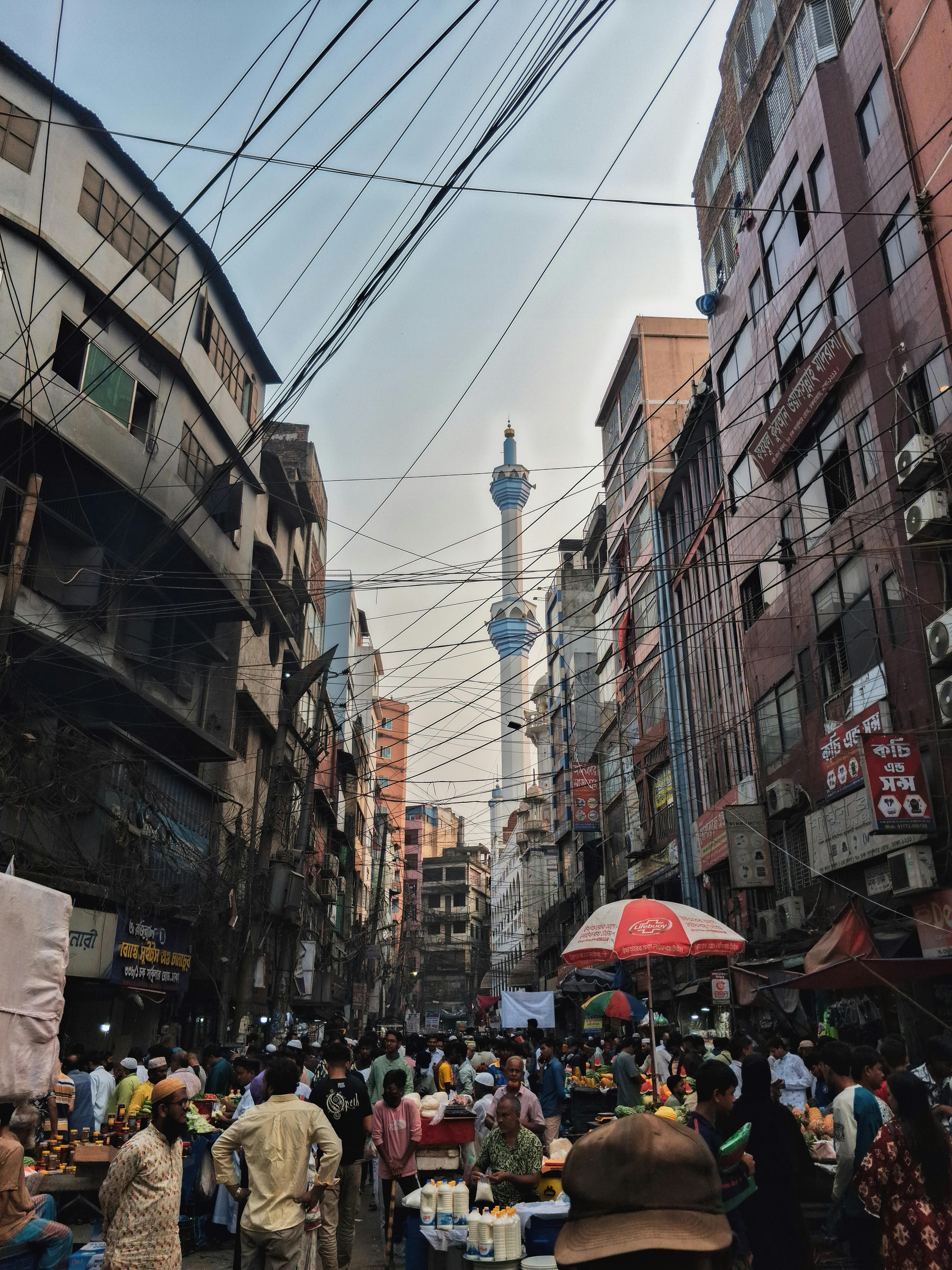 無料 賑やかなダッカのストリートマーケットの活気ある風景。背景にはモスクの塔があり、都市生活を表しています。 写真素材