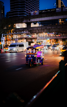 A vibrant tuk-tuk navigates through bustling evening traffic in Kuwait City, showcasing urban life.