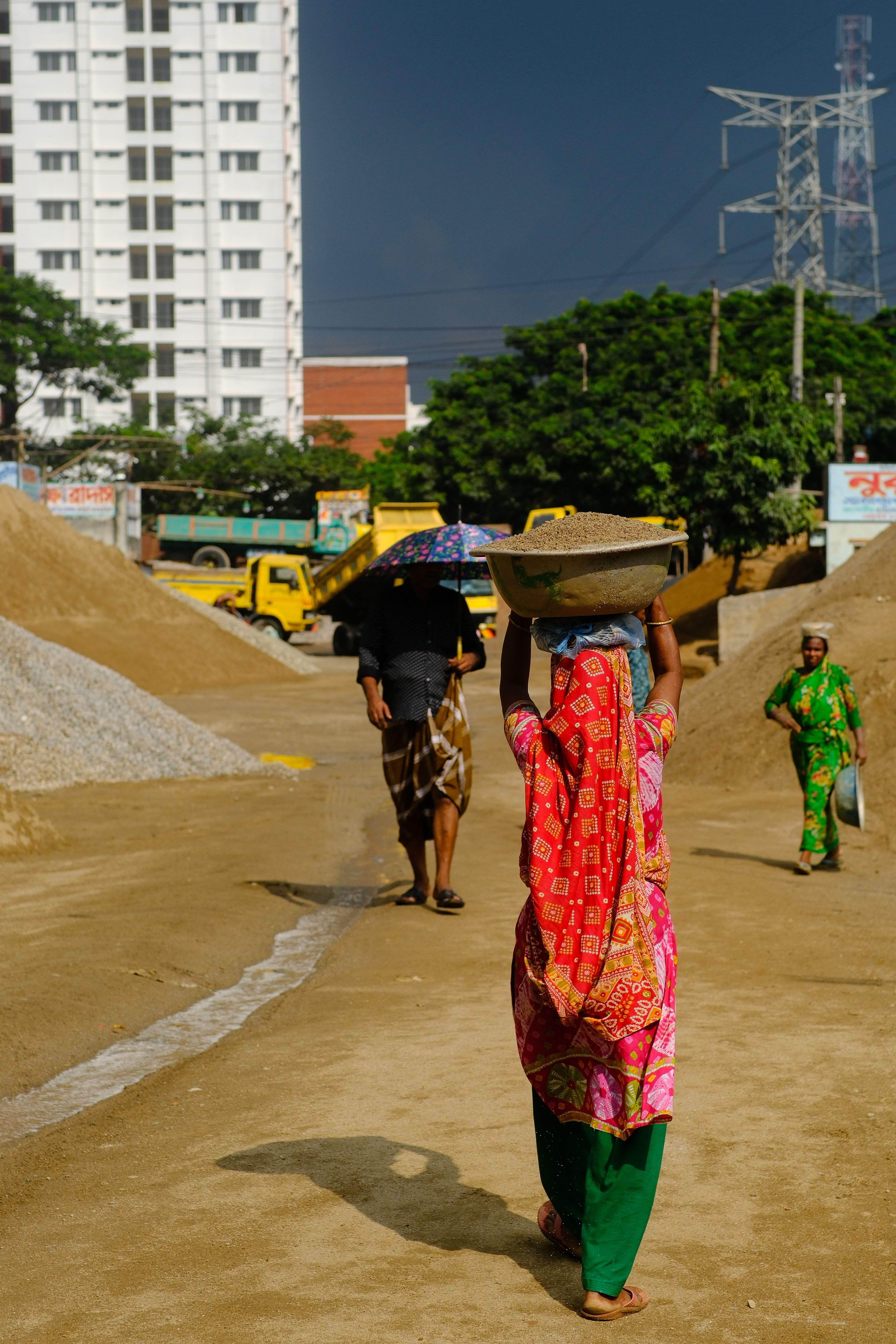 Construction workers carrying materials at an urban site under a sunny sky.
