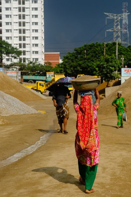 Construction workers carrying materials at an urban site under a sunny sky.