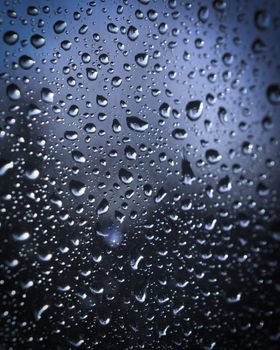 Abstract image of water droplets on a glass pane with a cool, moody tone.