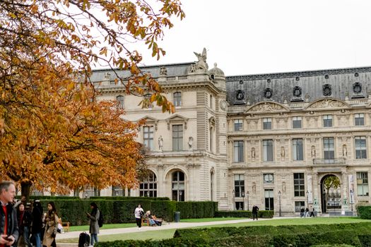 Beautiful autumn day at the Louvre Museum with people walking and trees in fall foliage.