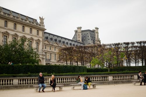 Free Visitors relax in front of the Louvre Museum, surrounded by lush greenery in Paris. Stock Photo