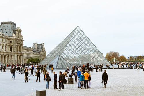 Free Tourists gather around the iconic Louvre Pyramid in Paris, highlighting European architecture. Stock Photo