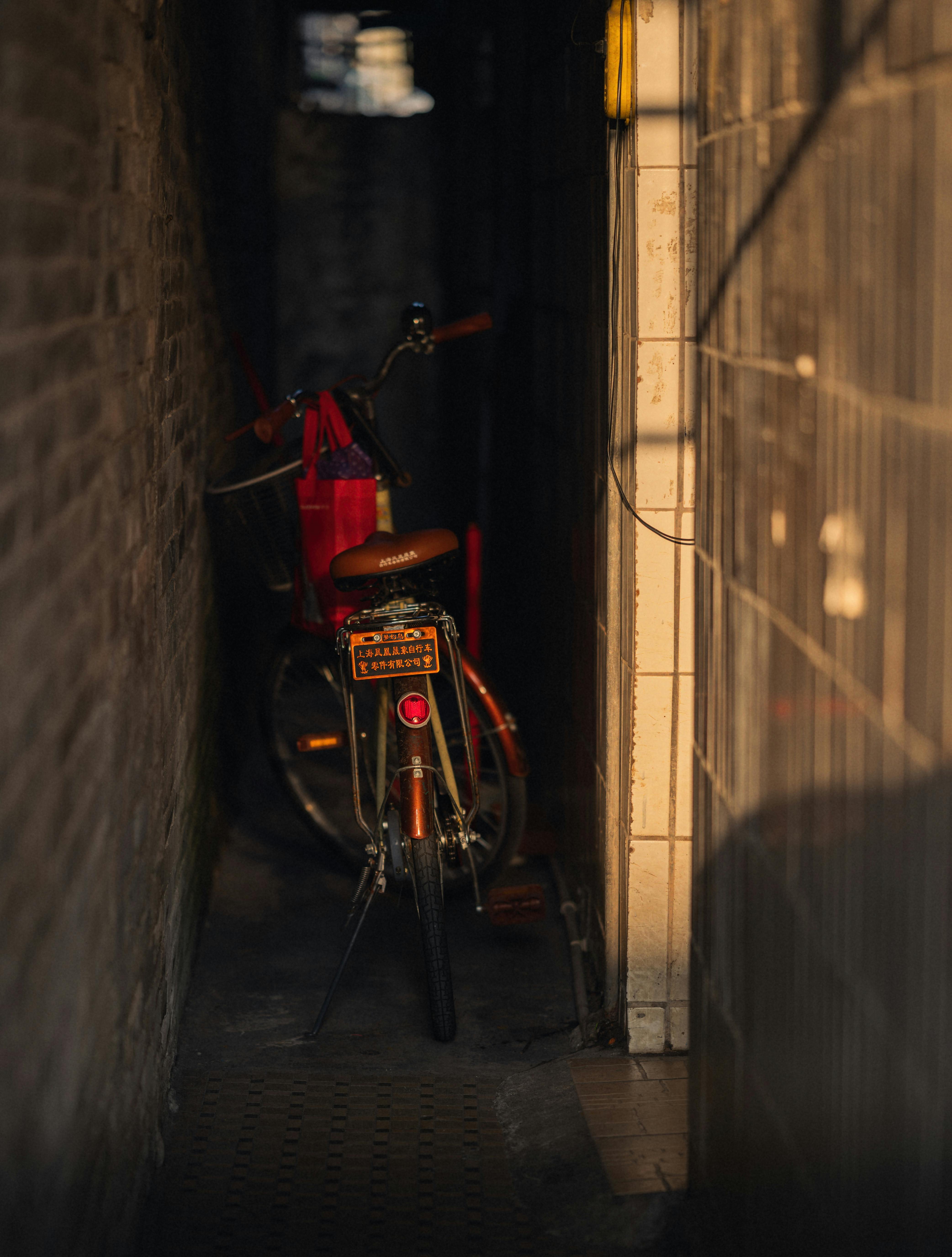De franc Una bicicleta està aparcada en un carreró urbà estret i mal il·luminat amb parets de maó, creant una atmosfera taciturna. Foto d'estoc