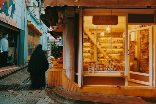 A cozy, warmly lit shopfront in a rainy street with a passerby and display mannequins.