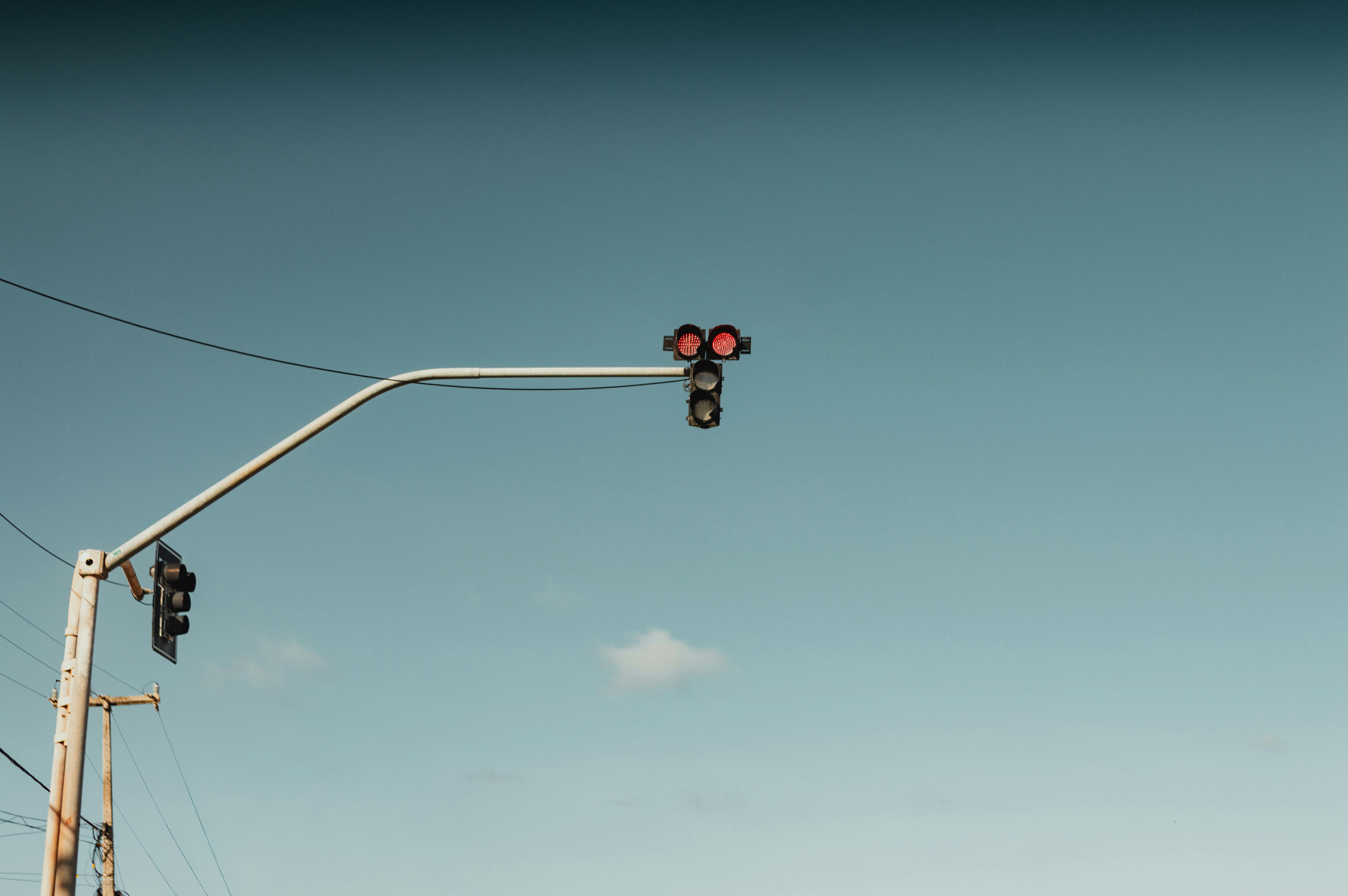 ฟรี สัญญาณไฟจราจรสีแดงตัดกับท้องฟ้าสีฟ้าสดใส แสดงถึงการหยุดและการระมัดระวังในสภาพแวดล้อมเมือง คลังภาพถ่าย