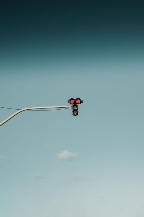 Free A minimalist photograph of a traffic light showing red lights against a clear blue sky. Stock Photo