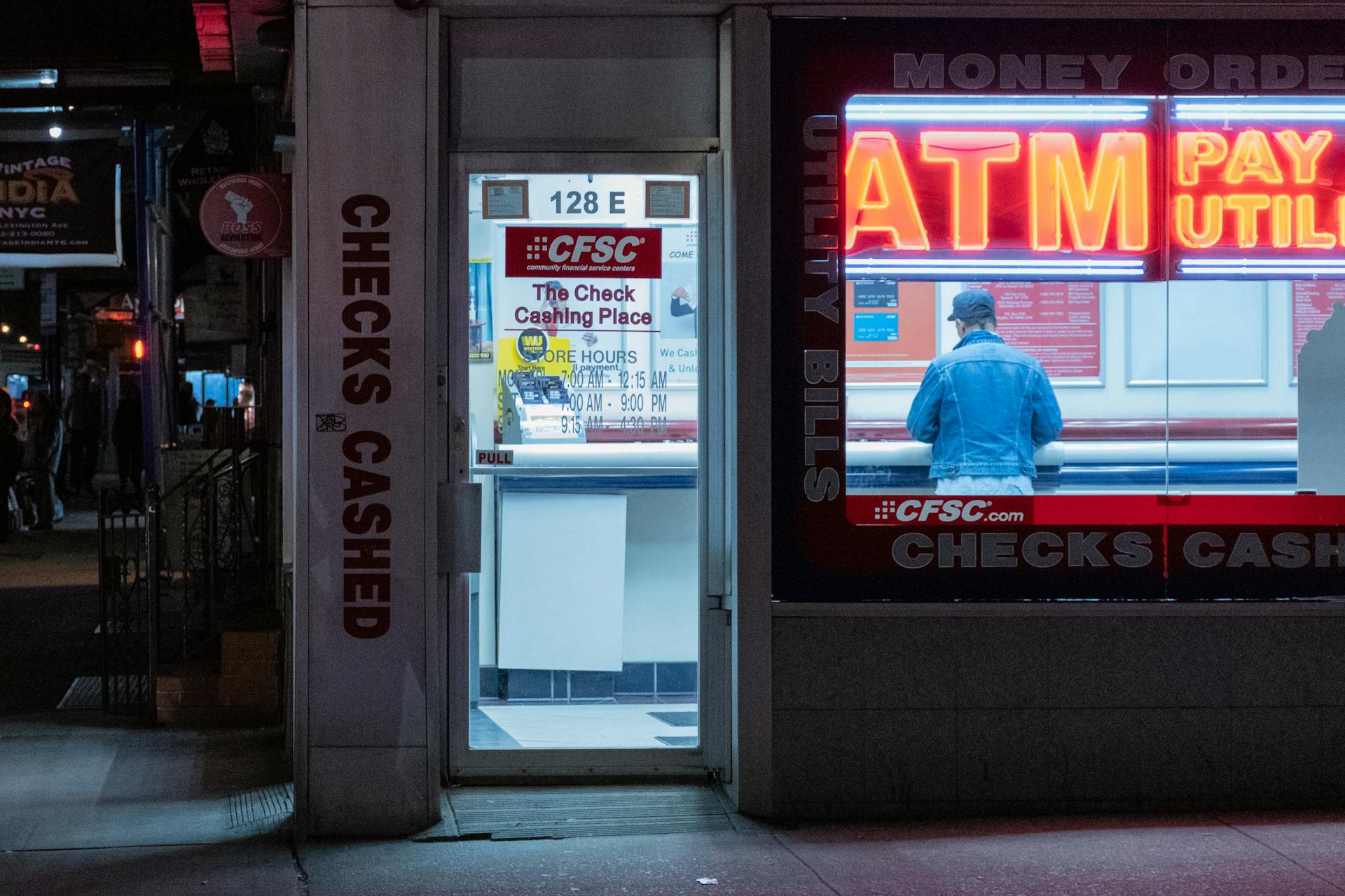 Neon-lit check cashing store with ATM services at night.