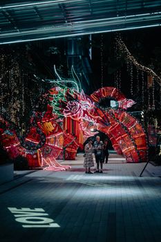 A colorful night festival scene featuring an illuminated dragon lantern with people enjoying the festive atmosphere.