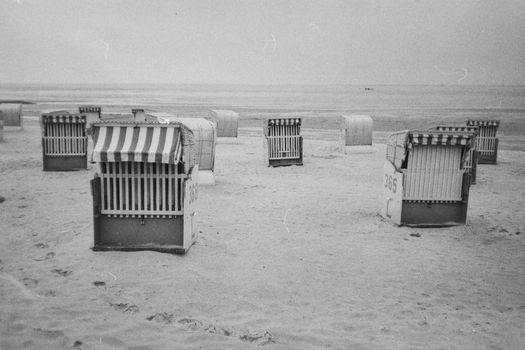 Black and white photo of empty beach chairs on a serene sandy shore.