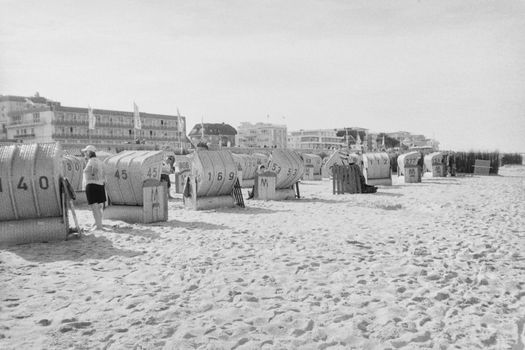 Vintage beach photo featuring wicker chairs lined up on the sand with people relaxing.