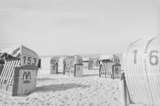 Black and white photo of vintage wicker beach chairs on a sandy beach.