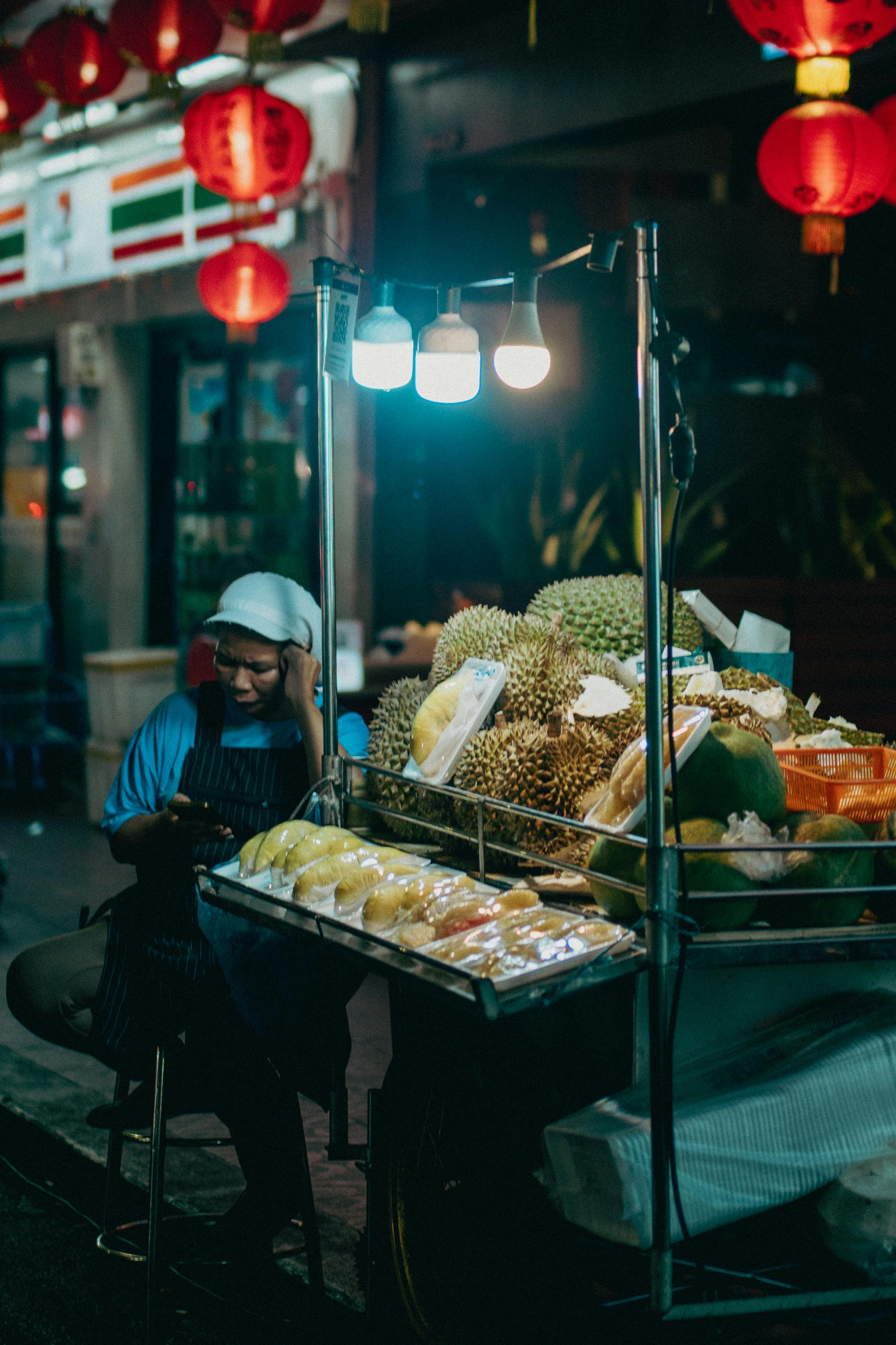 Street vendor at night market with tropical fruits under vibrant lights.