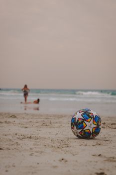 A vibrant soccer ball on a sandy beach with ocean waves at sunset in the background.