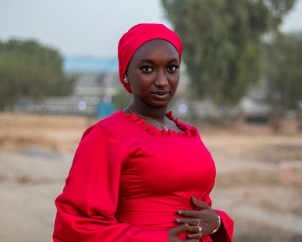 Portrait of a woman in a red hijab and dress, exuding confidence outdoors.