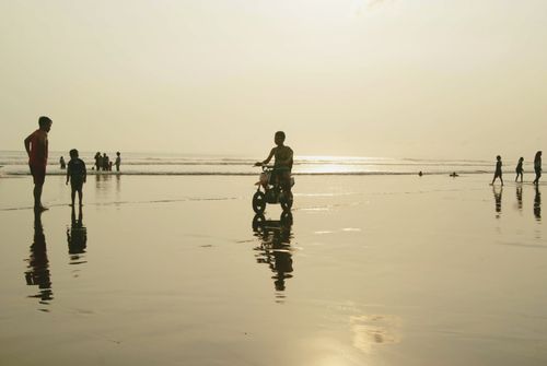Free Children play on Pangandaran Beach at sunset, reflecting silhouettes on wet sand. Stock Photo