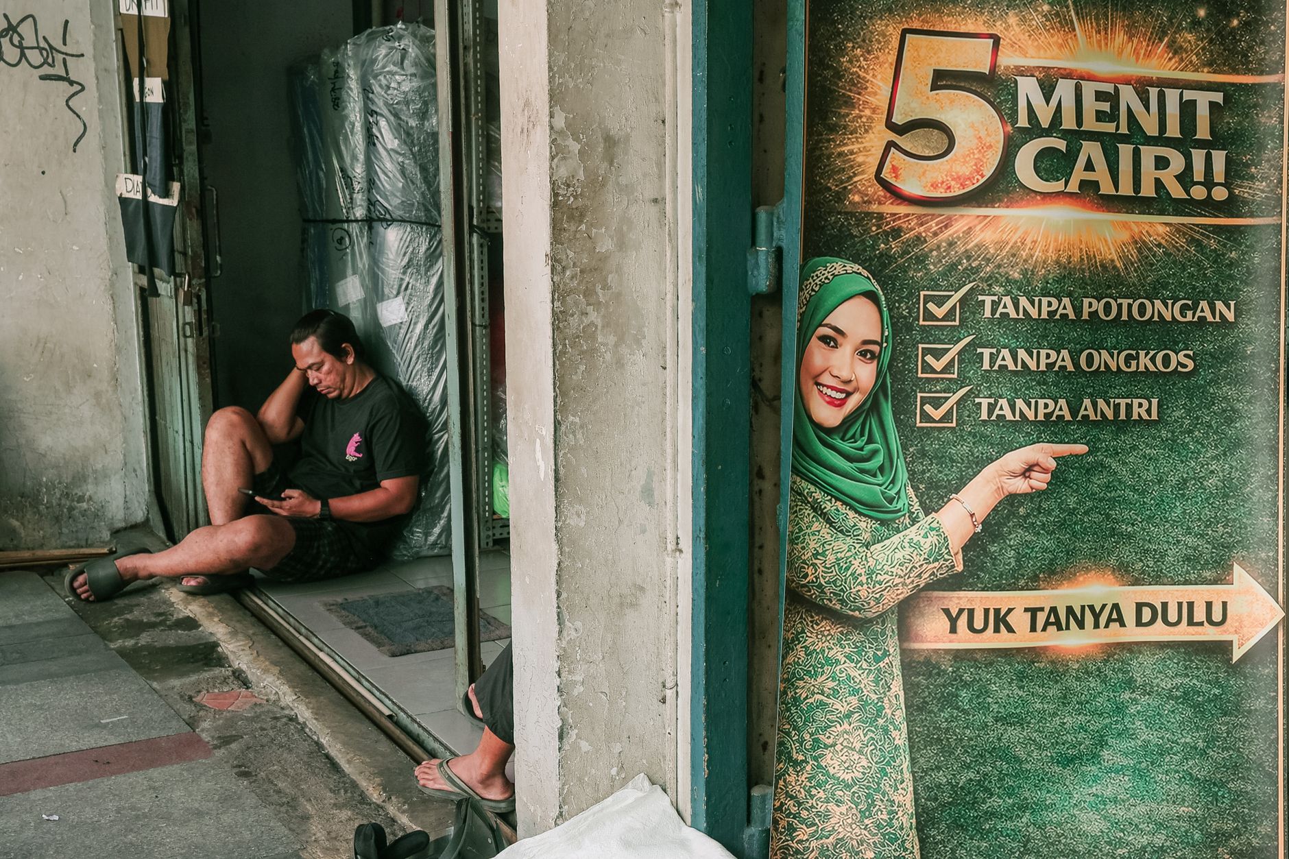 Street photograph in Bandung featuring a diverse marketing poster and a resting man.