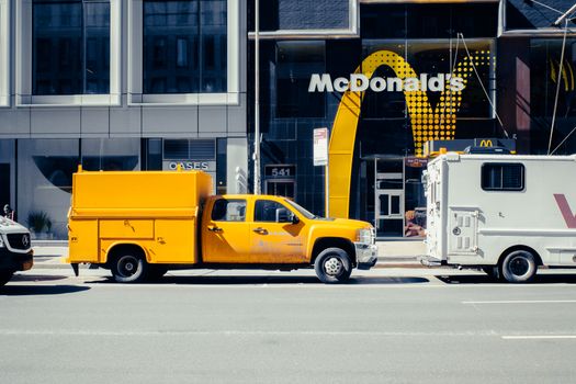 A yellow pickup truck parked in front of a McDonald's in New York City on a sunny day.