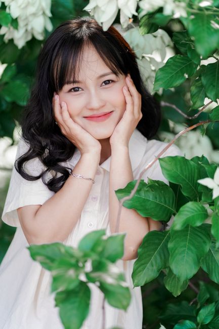 Cheerful woman posing amidst vibrant green foliage, exuding joy and warmth.