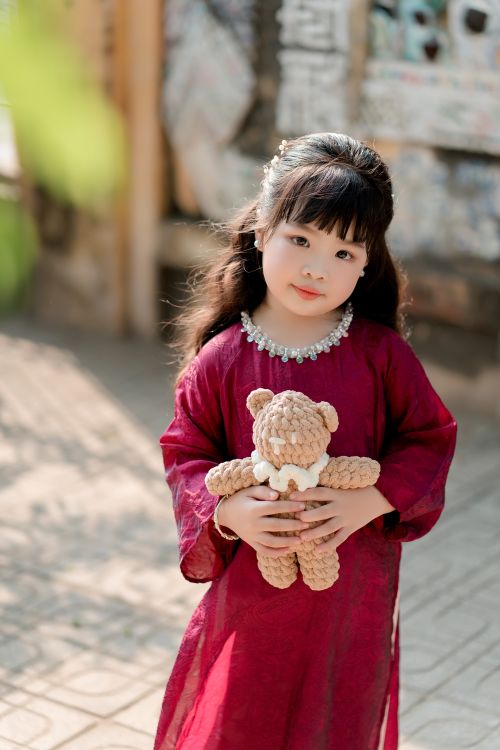 Free East Asian girl in a traditional red dress holding a teddy bear outdoors. Stock Photo