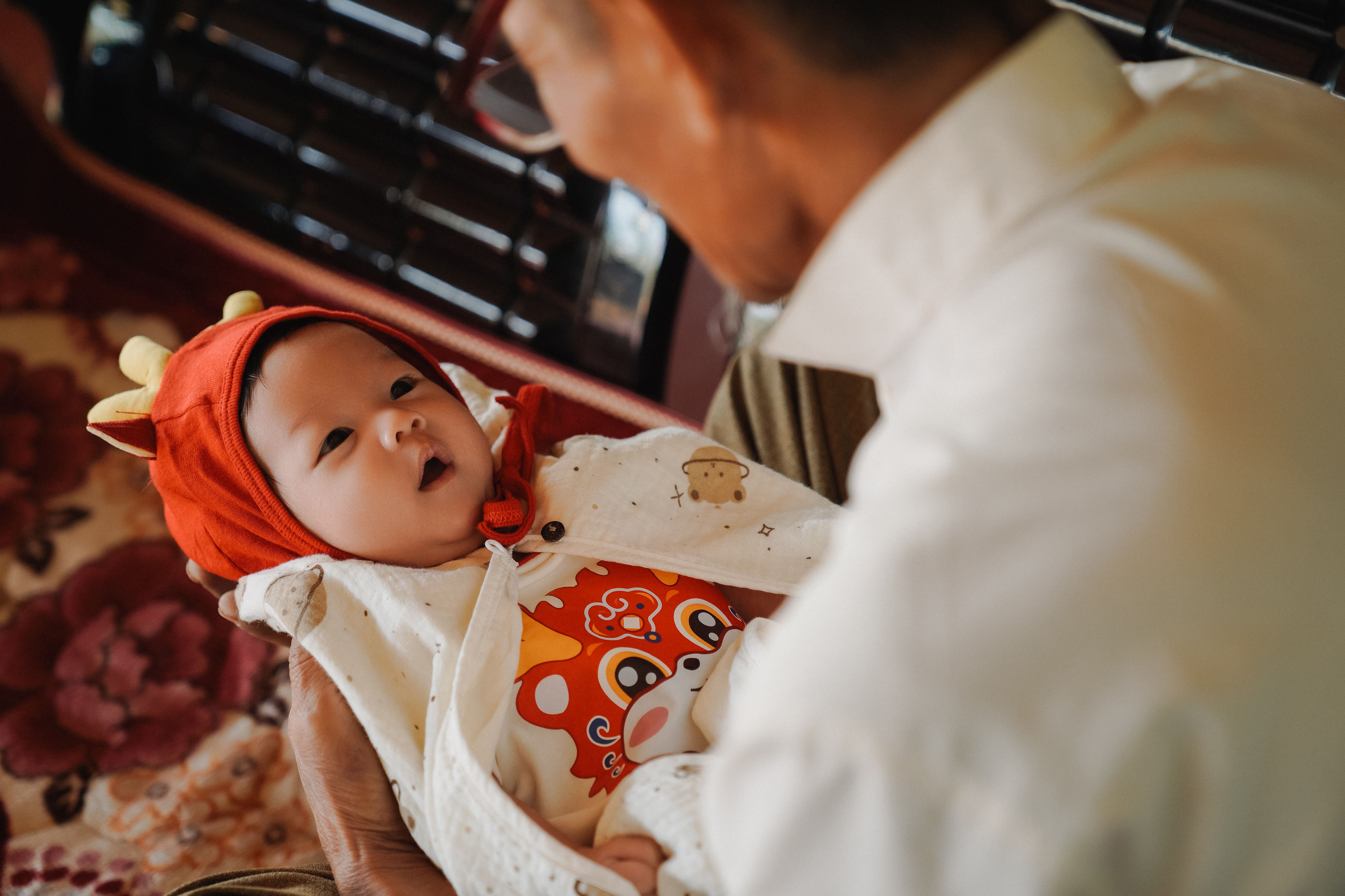 Un grand-parent berce un nouveau-né vêtu d'un adorable costume. Un tendre moment familial à l'intérieur.