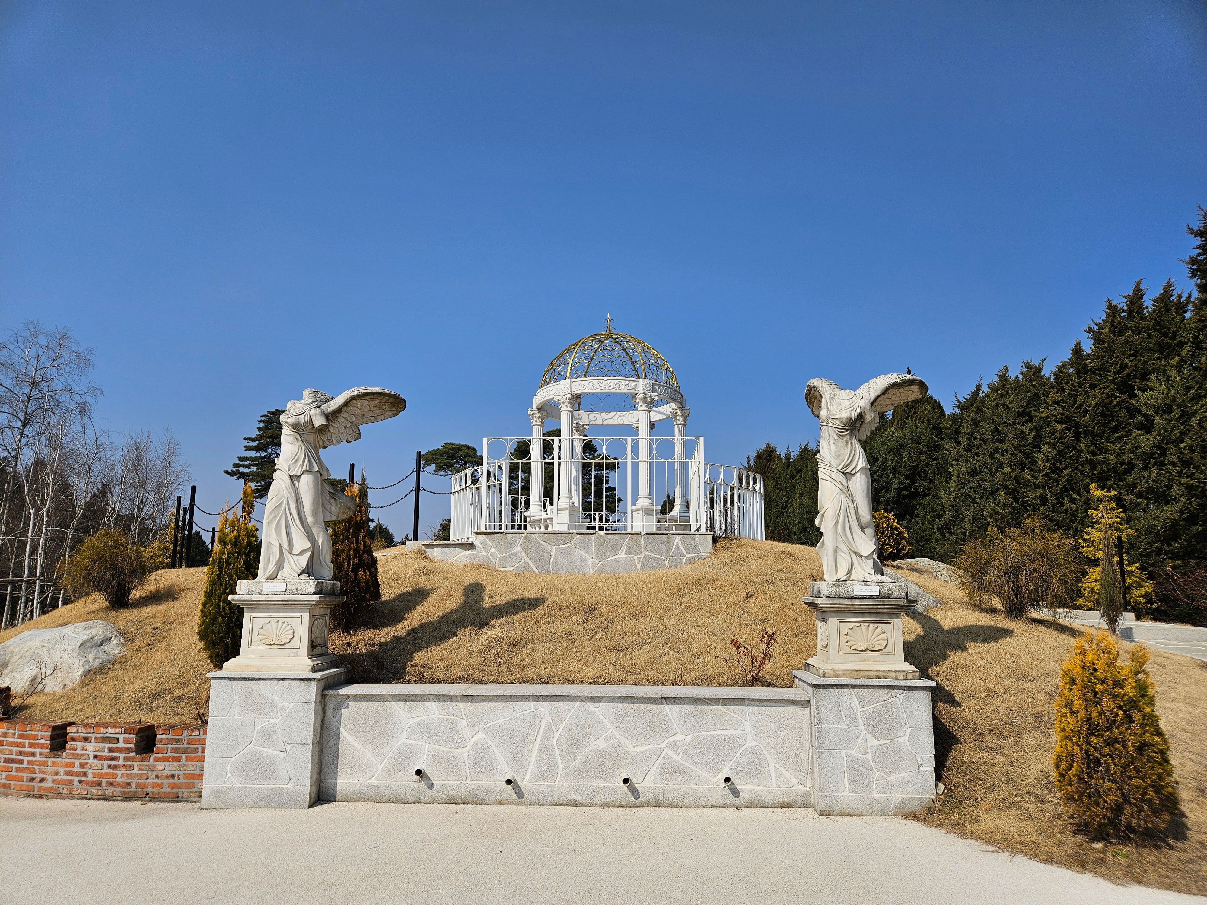 Graceful white pergola with angel statues in a serene Korean garden under a clear blue sky.