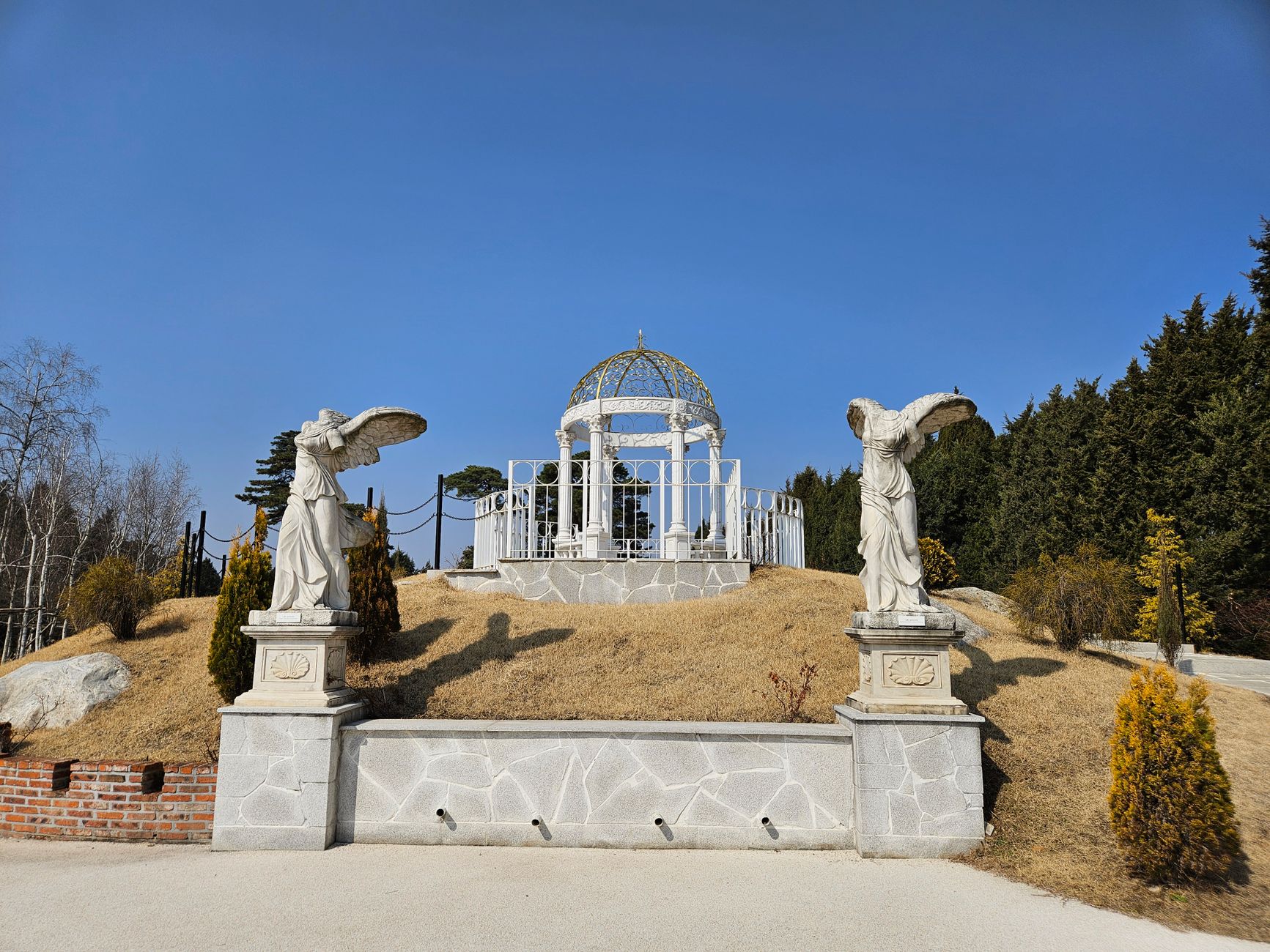Graceful white pergola with angel statues in a serene Korean garden under a clear blue sky.