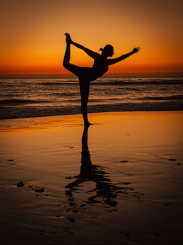 A serene silhouette of a woman practicing yoga on a Moroccan beach during sunset, reflecting tranquility.