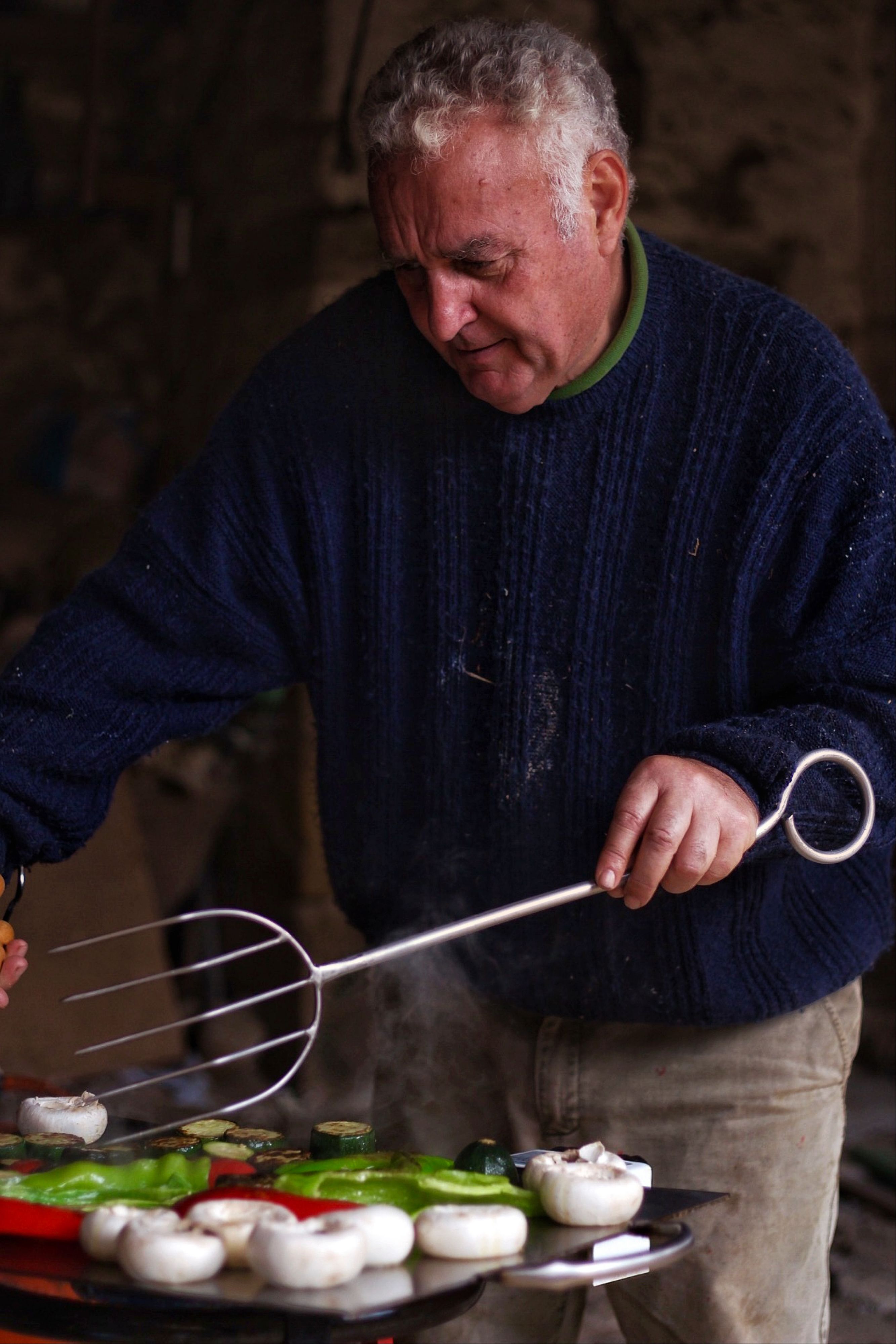 Senior man grilling vegetables and mushrooms outdoors, capturing a rustic culinary scene.