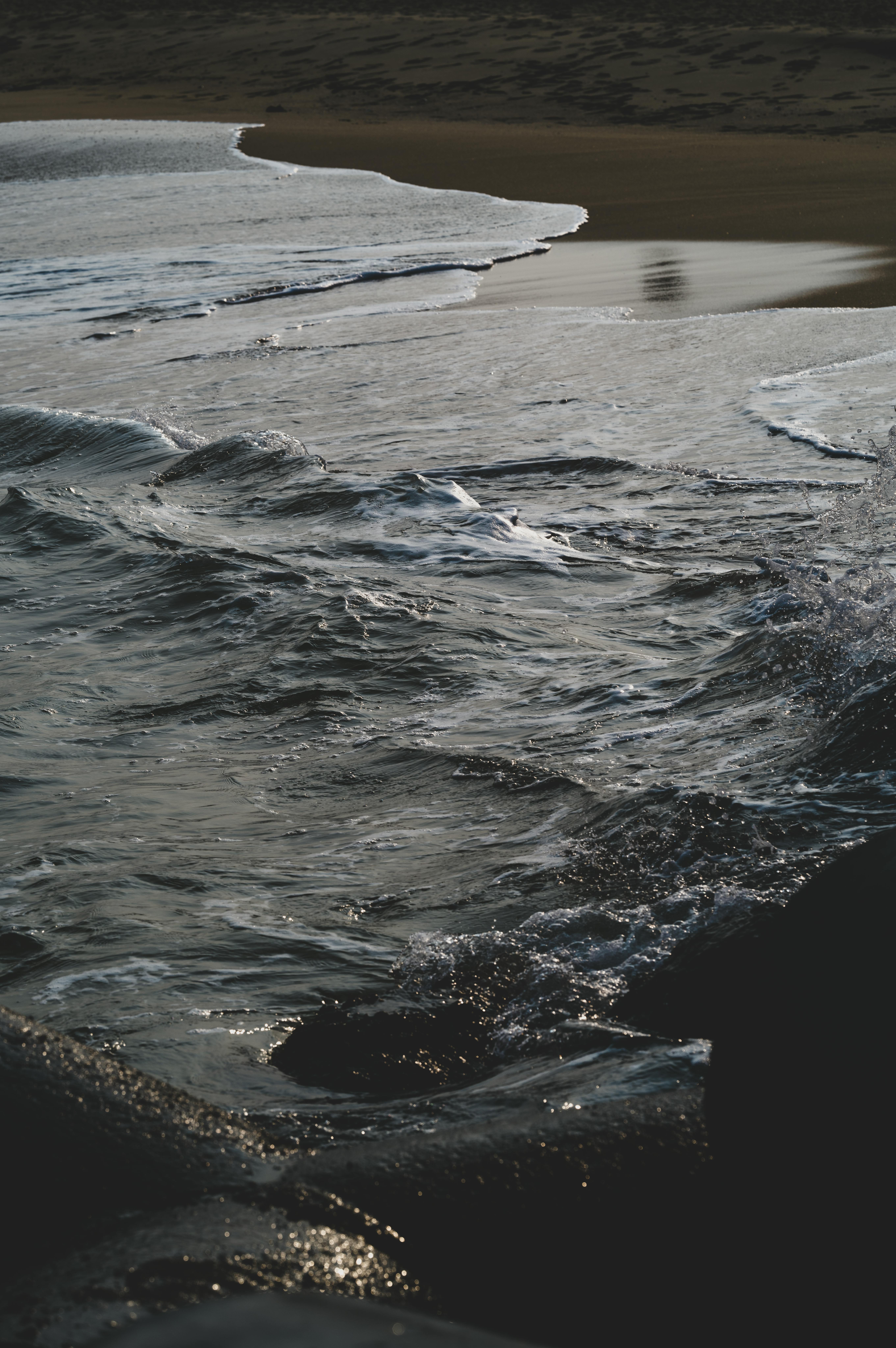 Ücretsiz Hafif dalgalar, hüzünlü bir gün batımı altında kıyıya vurarak sakin bir sahil manzarası sunuyor. Stok Fotoğraflar