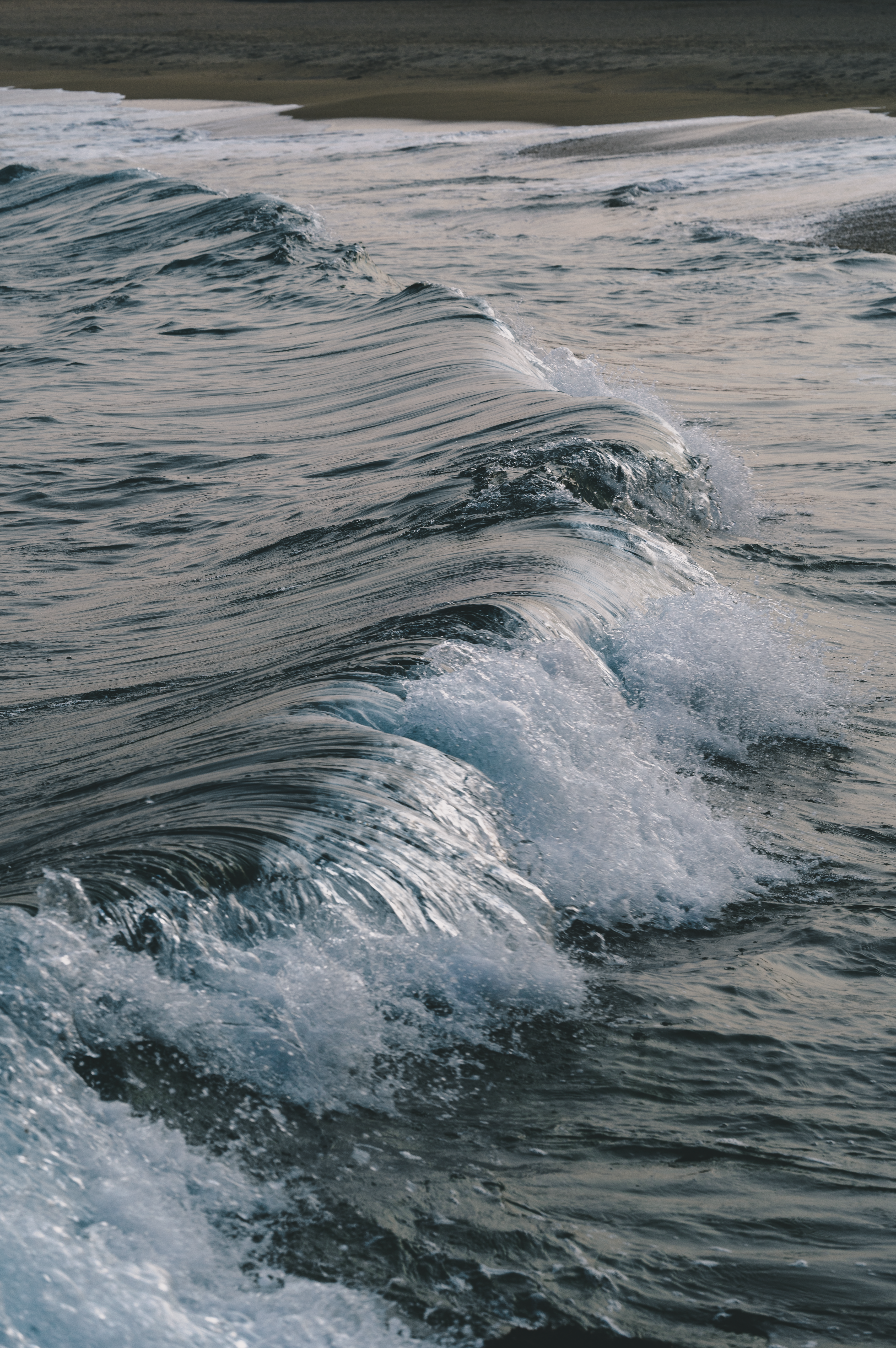 Tranquil ocean waves gently crashing on a sandy shore during the day.