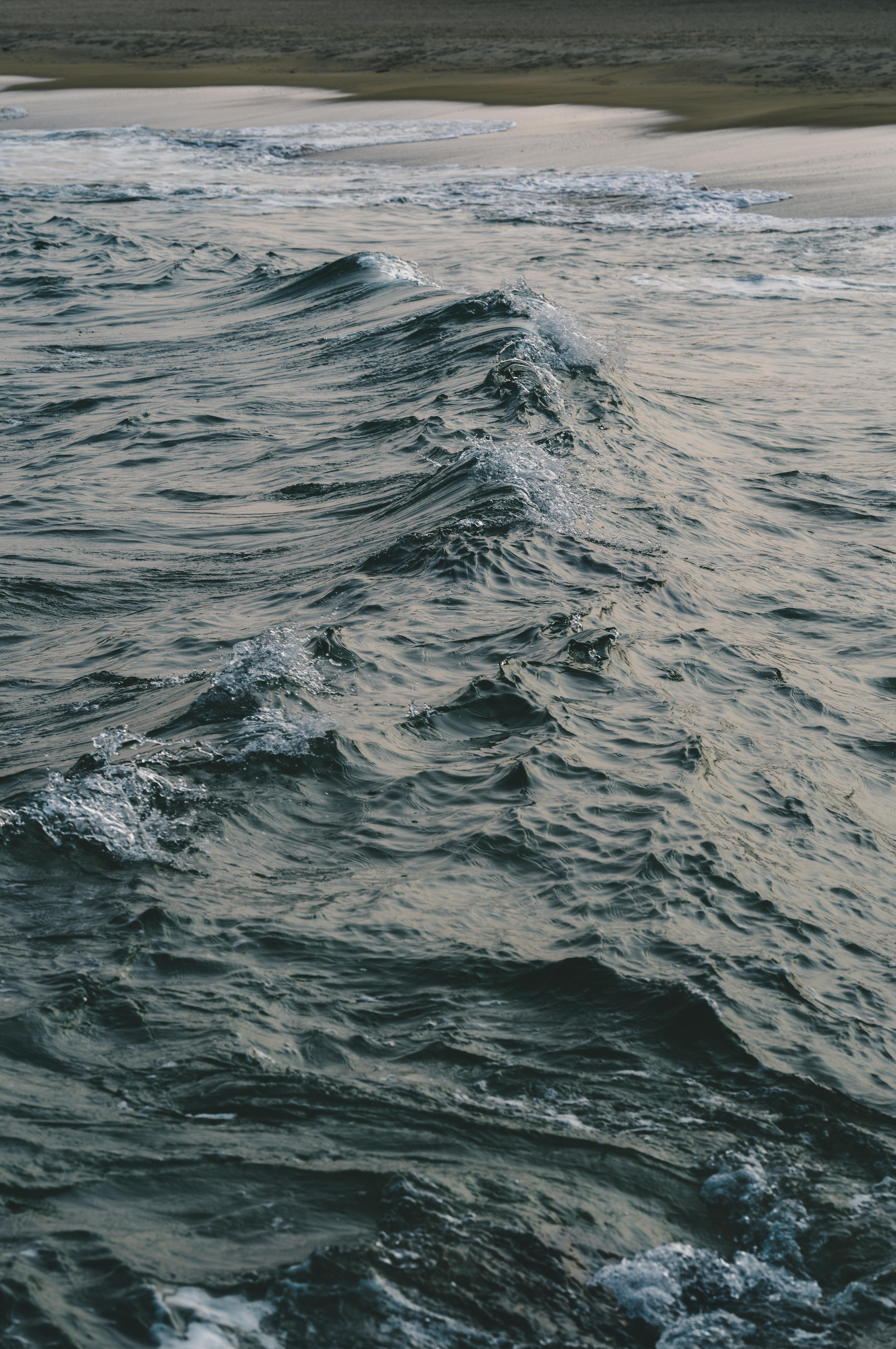 Ücretsiz Gün batımında okyanus dalgalarının kumlu bir kumsala nazikçe çarpışının huzurlu manzarası. Stok Fotoğraflar