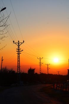 Beautiful sunset behind power lines creating a silhouette against a rural landscape.