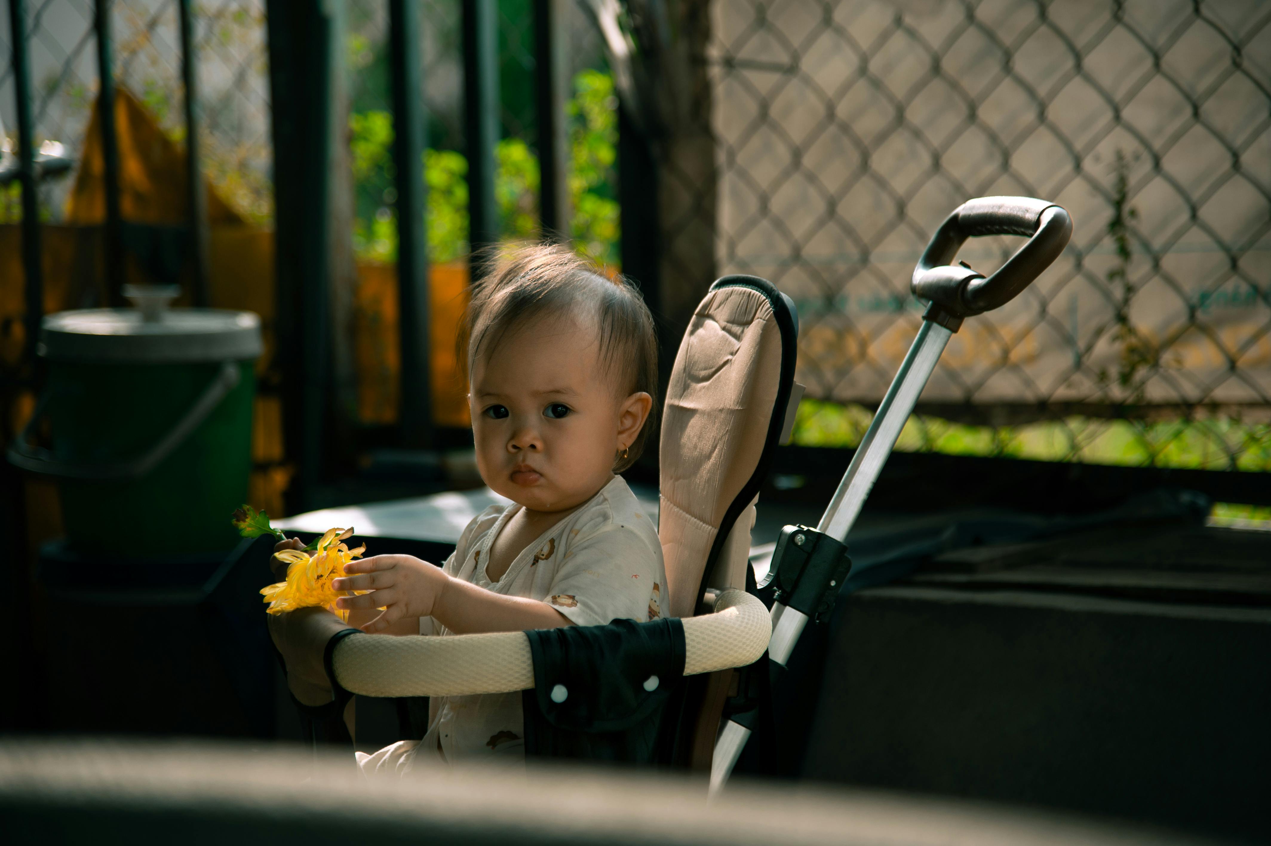 Charming baby sitting in a stroller holding a yellow flower in an outdoor setting.