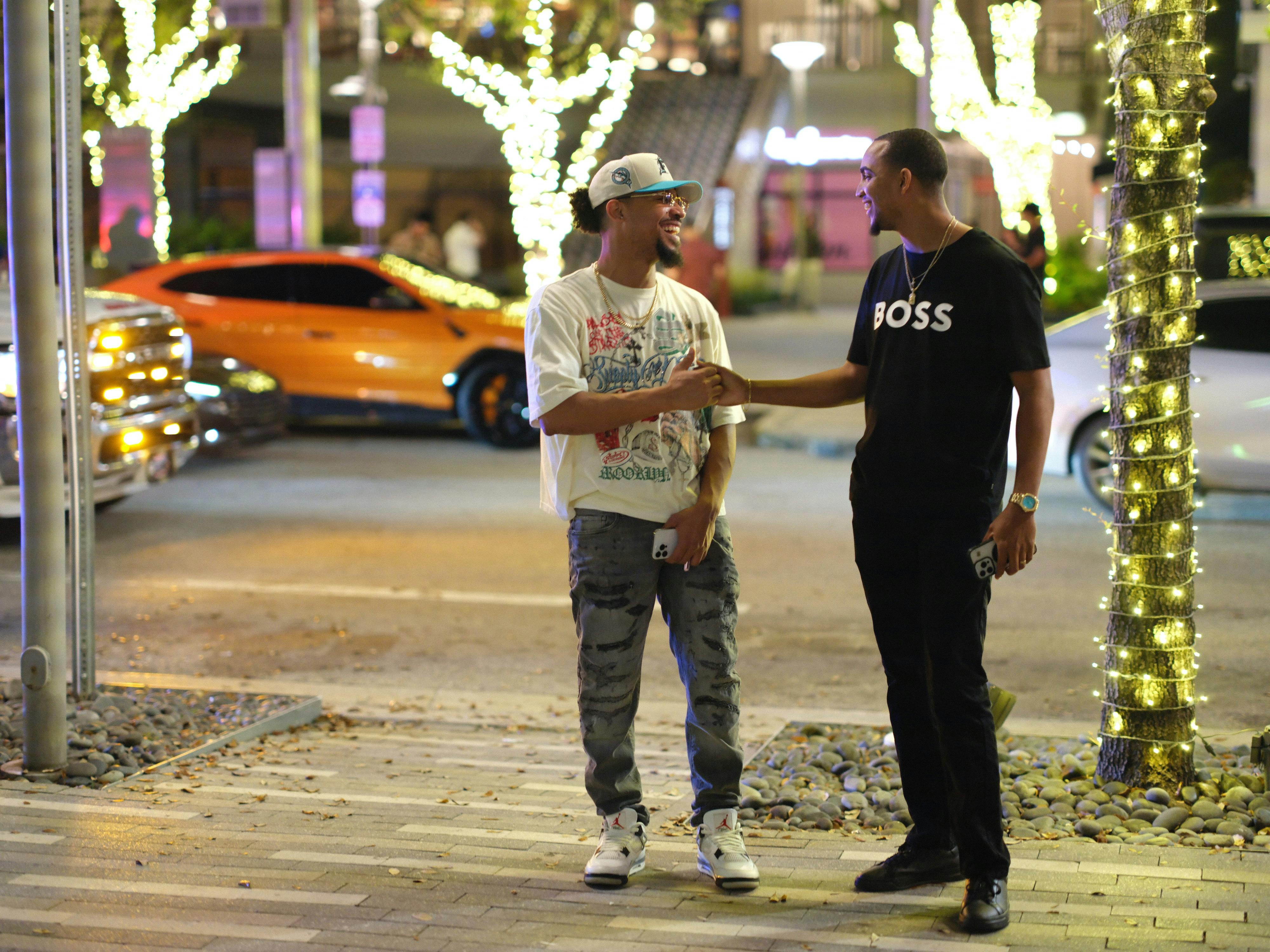 bezplatná Dva muži si vyměňují ruce na ulici plné nočního života v Miami na Floridě a demonstrují tak městské přátelství. Základová fotografie