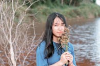 阳光明媚的日子里，一位身穿蓝色衬衫的亚洲妇女在河边捧着鲜花