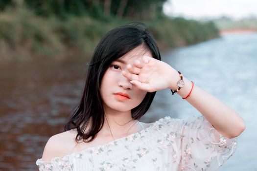 一名年轻女子在夏季的河边，手捂着脸的户外肖像