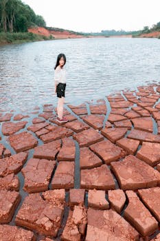 一名年轻女孩站在户外水体附近干裂的河床上