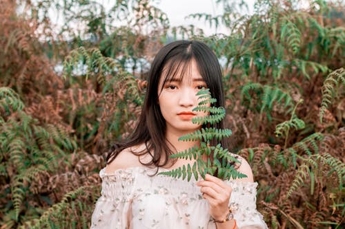 Photo De Mise Au Point Peu Profonde De Femme Portant Un Haut à Fleurs Blanc Tout En Tenant Des Feuilles De Fougère