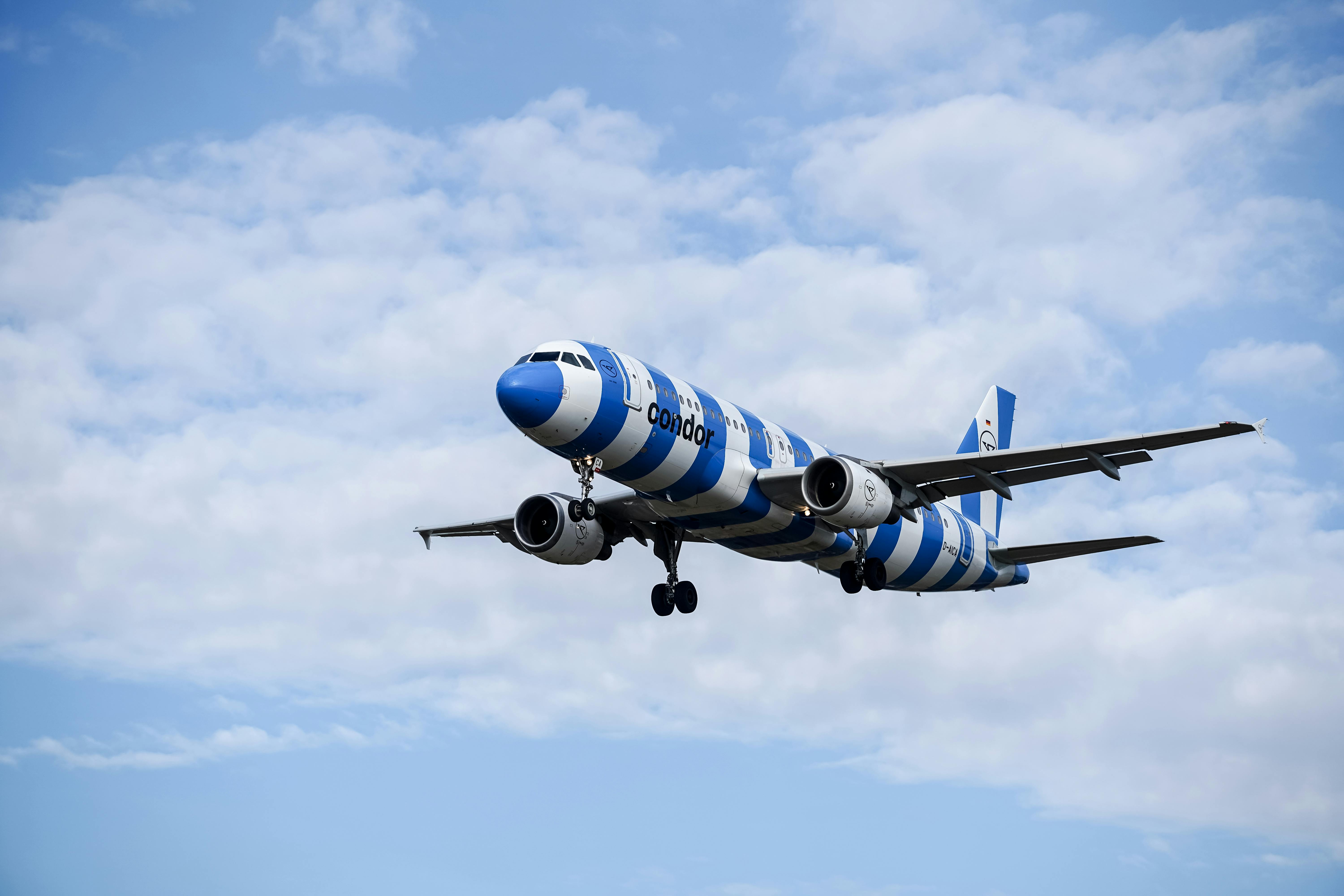 Airplane with blue and white stripes flying against a cloudy sky in Hamburg, Germany.