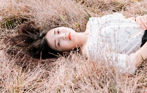 女人躺在棕色的草地上，穿着白色的花顶