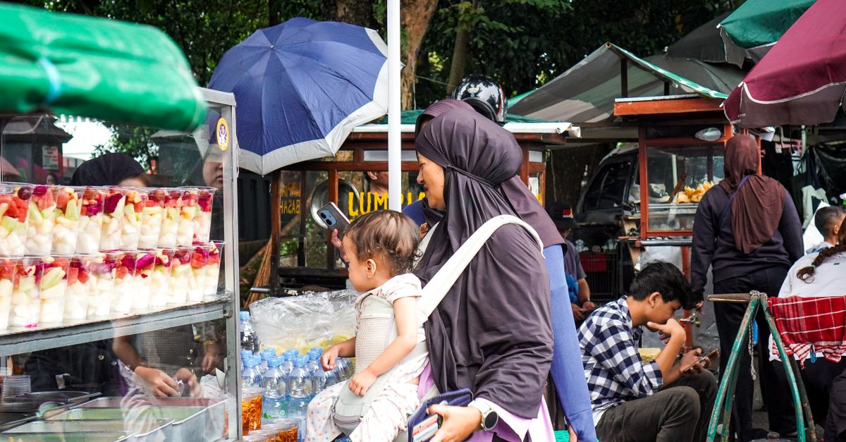 A vibrant scene at an outdoor market with people shopping under colorful umbrellas.