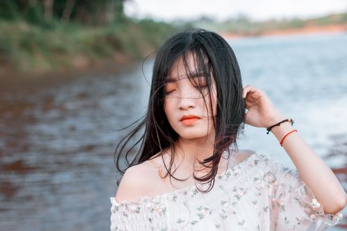 Free A woman peacefully posing by a riverside with wind-blown hair. Stock Photo